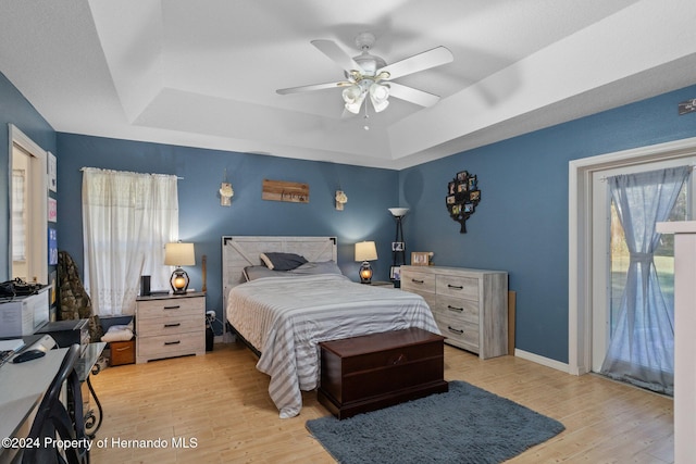 bedroom featuring ceiling fan, light hardwood / wood-style floors, and a tray ceiling