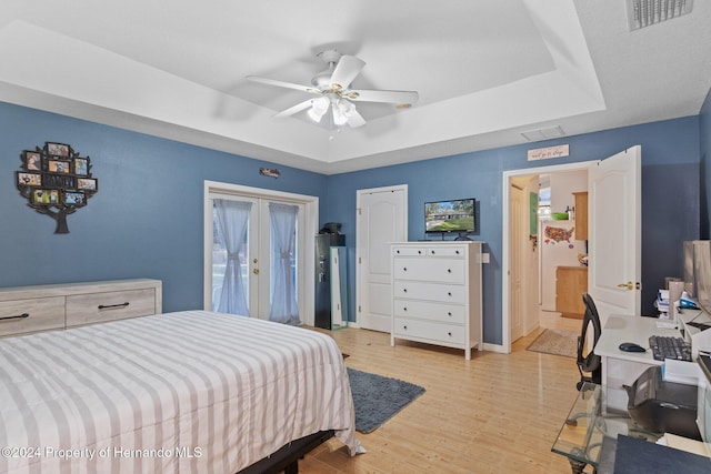 bedroom with a raised ceiling, ceiling fan, french doors, and light hardwood / wood-style floors