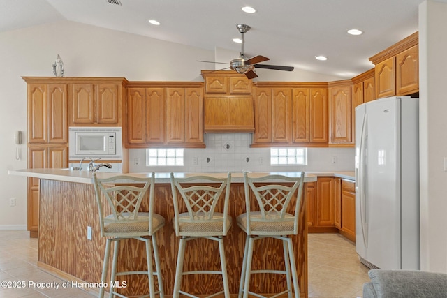 kitchen featuring a kitchen breakfast bar, vaulted ceiling, an island with sink, and white appliances