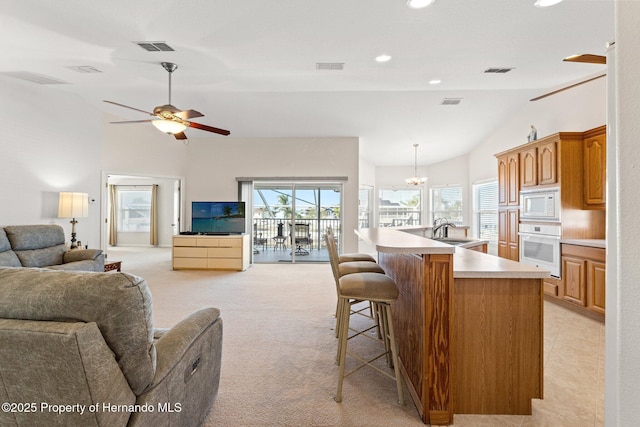 kitchen featuring lofted ceiling, a kitchen bar, a kitchen island with sink, light colored carpet, and white appliances