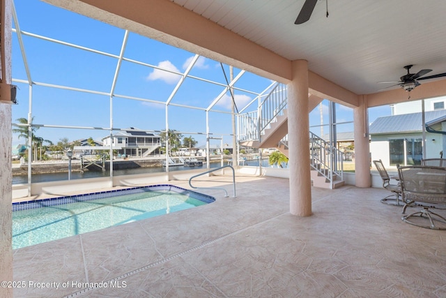 view of swimming pool featuring a patio, a water view, ceiling fan, and glass enclosure