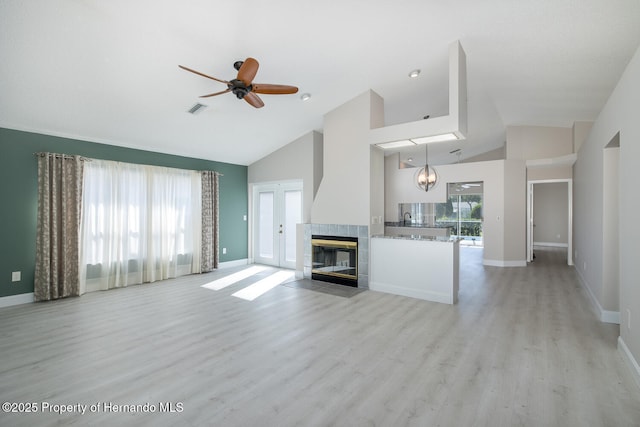 unfurnished living room featuring a healthy amount of sunlight, a tile fireplace, ceiling fan with notable chandelier, and light hardwood / wood-style flooring