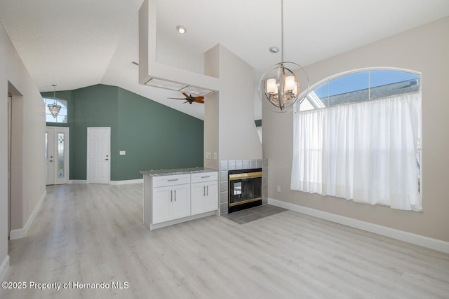 kitchen featuring decorative light fixtures, a tile fireplace, ceiling fan with notable chandelier, white cabinetry, and light stone counters