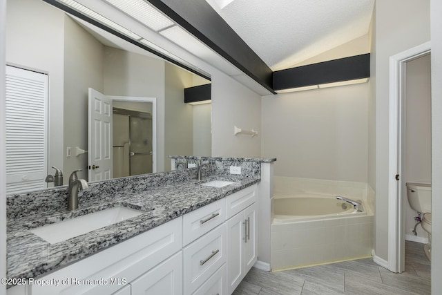 bathroom with a textured ceiling, lofted ceiling, tiled tub, vanity, and toilet