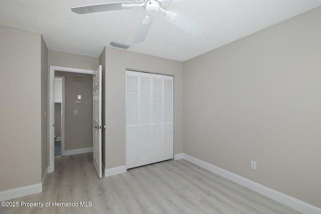 unfurnished bedroom with ceiling fan, a closet, a textured ceiling, and light hardwood / wood-style floors