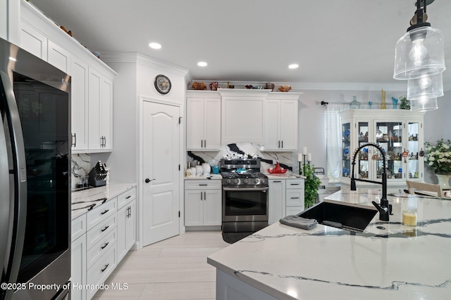 kitchen with light stone countertops, appliances with stainless steel finishes, sink, decorative light fixtures, and white cabinetry