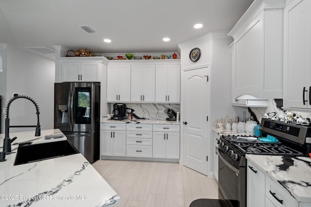 kitchen with light stone counters, stainless steel appliances, white cabinetry, and sink