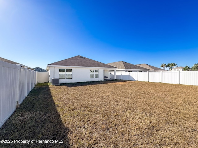 rear view of house featuring central AC unit and a lawn