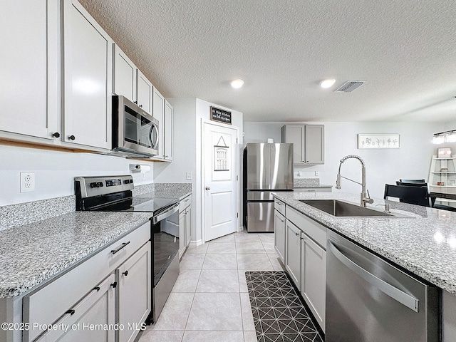 kitchen with a kitchen island with sink, sink, light tile patterned floors, light stone counters, and stainless steel appliances