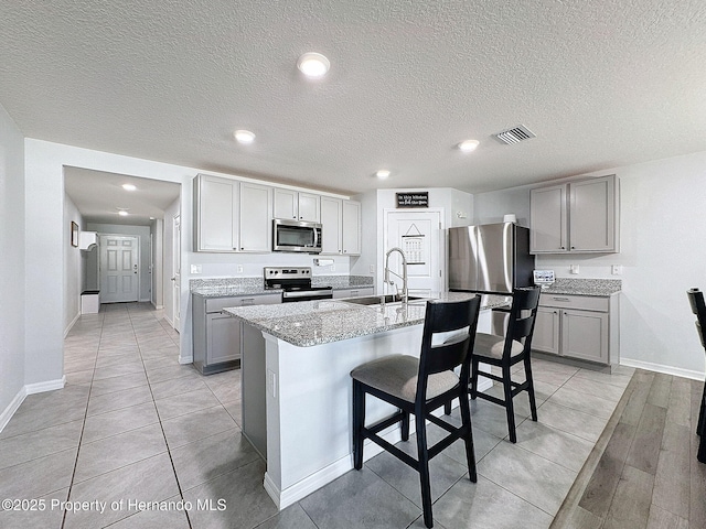 kitchen featuring a kitchen island with sink, sink, light stone countertops, a kitchen bar, and stainless steel appliances