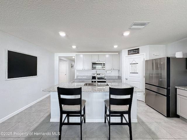 kitchen featuring a center island with sink, light tile patterned flooring, light stone countertops, and appliances with stainless steel finishes