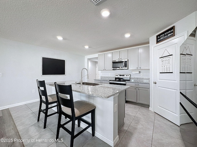 kitchen featuring gray cabinetry, sink, light stone countertops, an island with sink, and stainless steel appliances