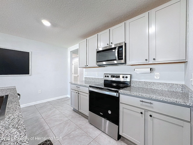 kitchen featuring white cabinets, a textured ceiling, stainless steel appliances, and light stone counters