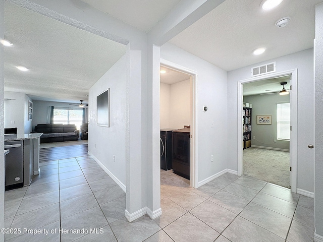 corridor with washing machine and dryer, light tile patterned flooring, and a textured ceiling