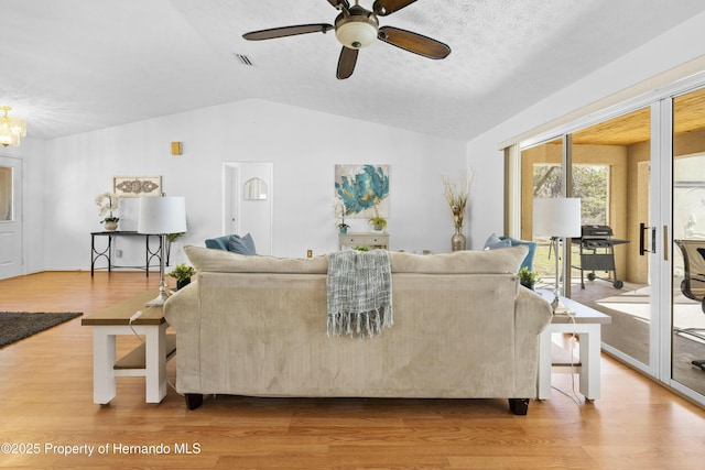 living room with ceiling fan with notable chandelier, vaulted ceiling, and light hardwood / wood-style flooring