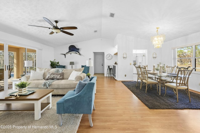 living room featuring ceiling fan with notable chandelier, light wood-type flooring, plenty of natural light, and lofted ceiling