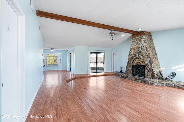 unfurnished living room featuring a textured ceiling, ceiling fan, lofted ceiling with beams, hardwood / wood-style floors, and a stone fireplace