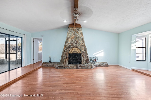 unfurnished living room with hardwood / wood-style floors, lofted ceiling, a stone fireplace, ceiling fan, and a textured ceiling