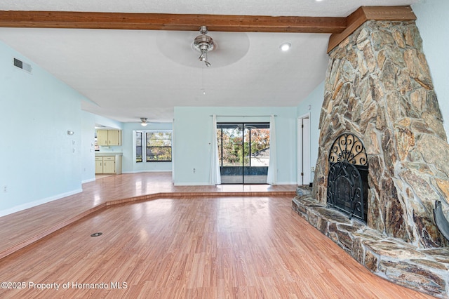 unfurnished living room featuring hardwood / wood-style floors, lofted ceiling with beams, a stone fireplace, and ceiling fan