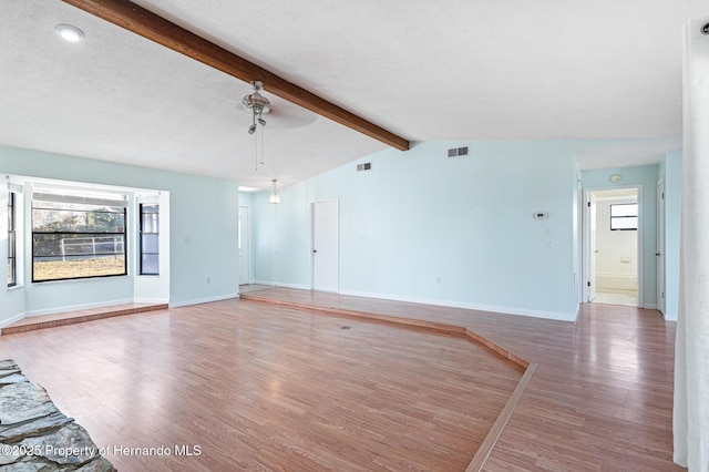 unfurnished living room with lofted ceiling with beams, ceiling fan, wood-type flooring, and a textured ceiling