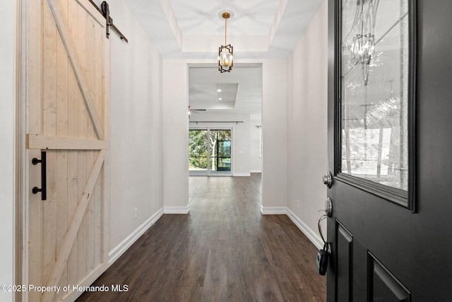 foyer entrance with ceiling fan, a barn door, dark hardwood / wood-style flooring, and a tray ceiling