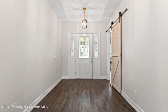 foyer with a tray ceiling, a barn door, and dark hardwood / wood-style flooring