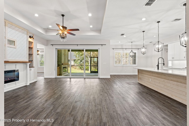 unfurnished living room with ceiling fan, sink, dark hardwood / wood-style flooring, a tray ceiling, and a fireplace