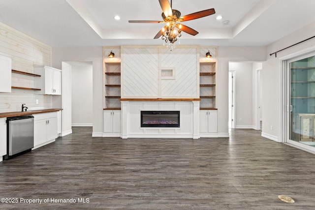 unfurnished living room with a tray ceiling, ceiling fan, and dark wood-type flooring