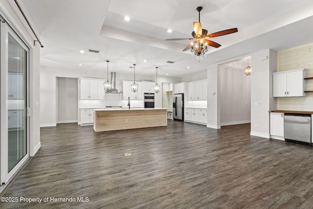 kitchen featuring tasteful backsplash, a tray ceiling, an island with sink, and appliances with stainless steel finishes