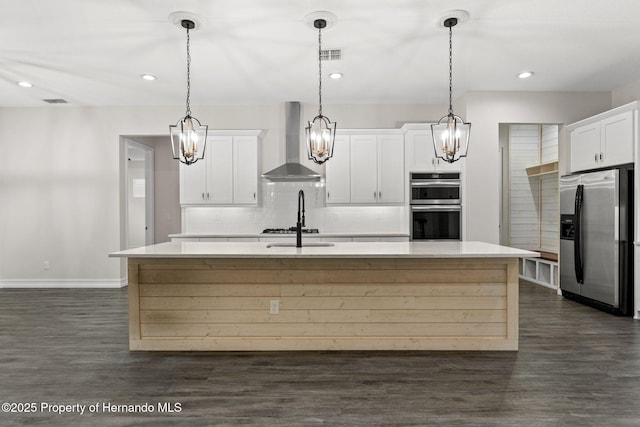 kitchen with white cabinetry, a kitchen island with sink, stainless steel appliances, and wall chimney range hood