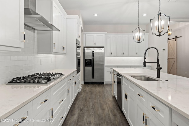 kitchen with white cabinets, appliances with stainless steel finishes, a barn door, and wall chimney exhaust hood