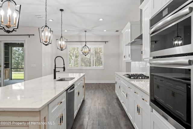 kitchen with a large island with sink, white cabinets, hanging light fixtures, sink, and stainless steel appliances