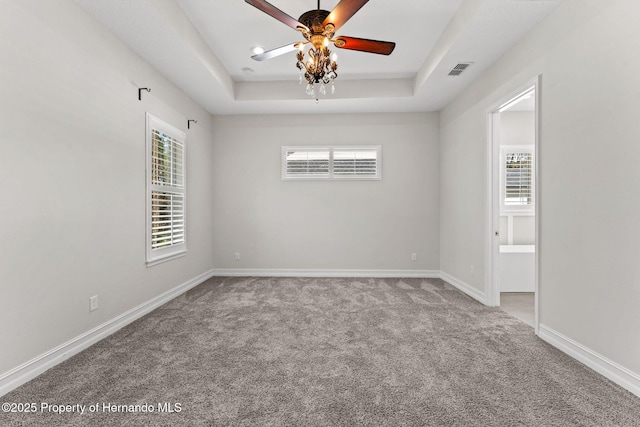 carpeted spare room featuring a tray ceiling, ceiling fan, and plenty of natural light