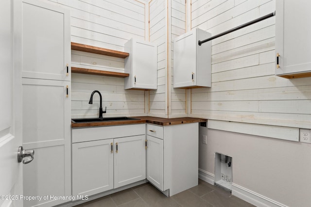 kitchen featuring white cabinetry, sink, wood counters, tile patterned flooring, and wood walls