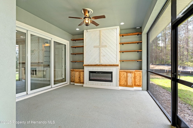 unfurnished sunroom with ceiling fan and a large fireplace