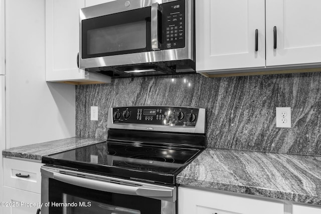 kitchen featuring white cabinets, appliances with stainless steel finishes, and dark stone counters