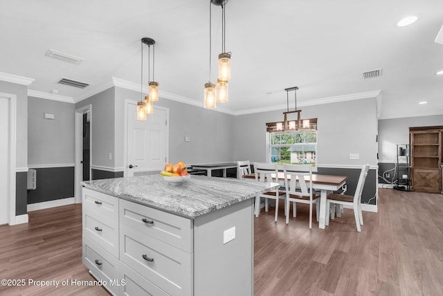 kitchen featuring white cabinets, crown molding, hanging light fixtures, light wood-type flooring, and a kitchen island