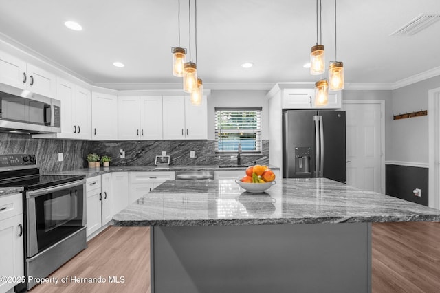 kitchen with white cabinets, appliances with stainless steel finishes, pendant lighting, a kitchen island, and ornamental molding