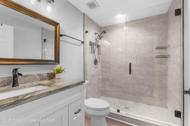 bathroom featuring a shower with door, vanity, and toilet