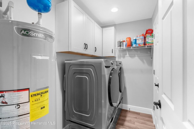 clothes washing area with cabinets, washing machine and dryer, hardwood / wood-style flooring, and water heater