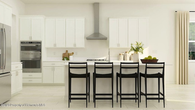 kitchen with double oven, a kitchen bar, white cabinets, and wall chimney range hood