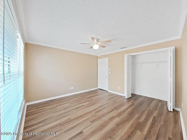 unfurnished bedroom with a textured ceiling, ceiling fan, crown molding, hardwood / wood-style flooring, and a closet