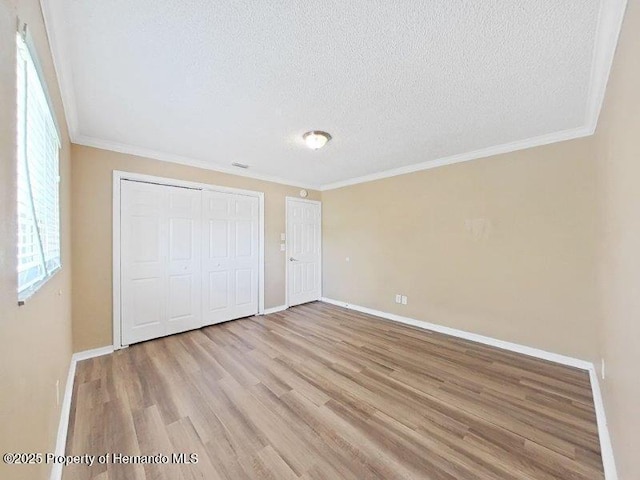 unfurnished bedroom featuring a textured ceiling, light hardwood / wood-style floors, multiple windows, and ornamental molding