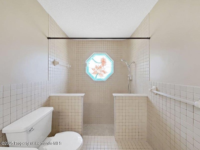 bathroom with tiled shower, a textured ceiling, toilet, and tile walls