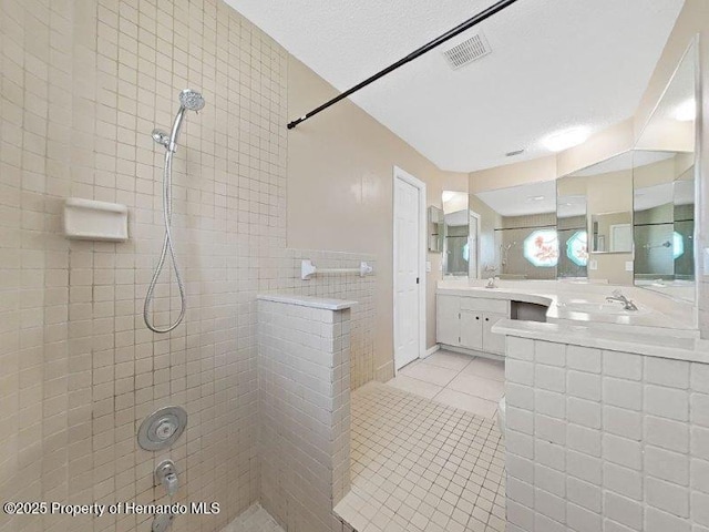 bathroom with tile patterned floors, vanity, a textured ceiling, and tiled shower