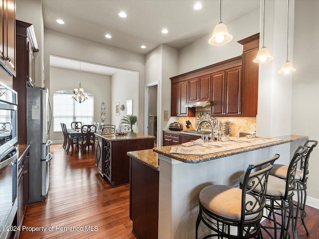 kitchen featuring hanging light fixtures, light stone counters, kitchen peninsula, stainless steel refrigerator, and a chandelier