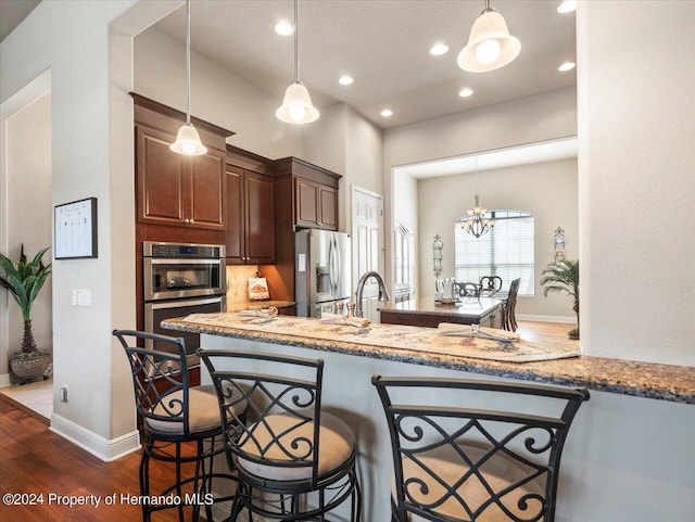 kitchen with stainless steel appliances, a notable chandelier, kitchen peninsula, pendant lighting, and a breakfast bar