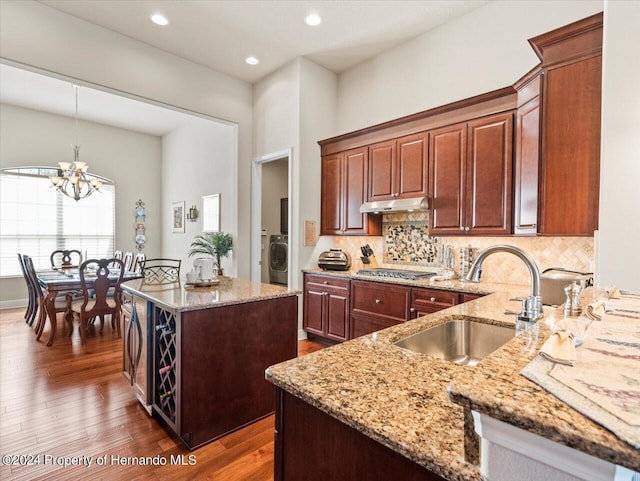 kitchen featuring stainless steel gas cooktop, sink, a notable chandelier, washer / dryer, and hanging light fixtures