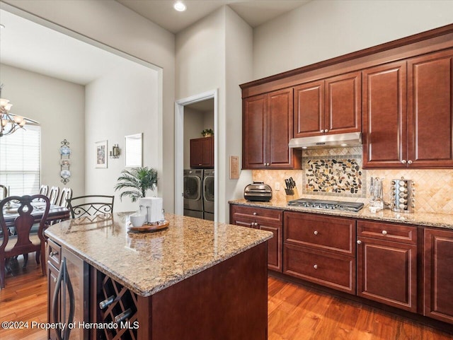 kitchen with light stone countertops, a notable chandelier, independent washer and dryer, stainless steel gas stovetop, and a kitchen island