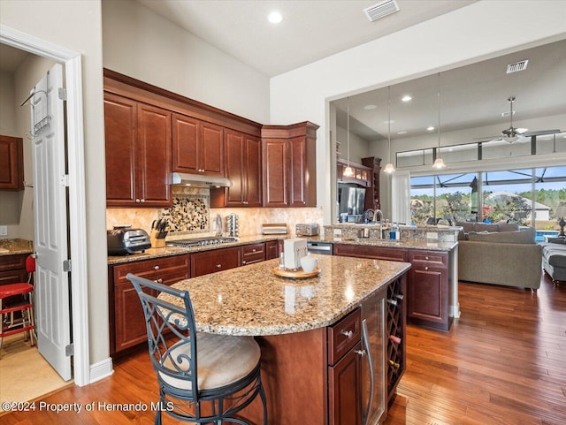 kitchen featuring ceiling fan, kitchen peninsula, pendant lighting, stainless steel gas stovetop, and a kitchen island